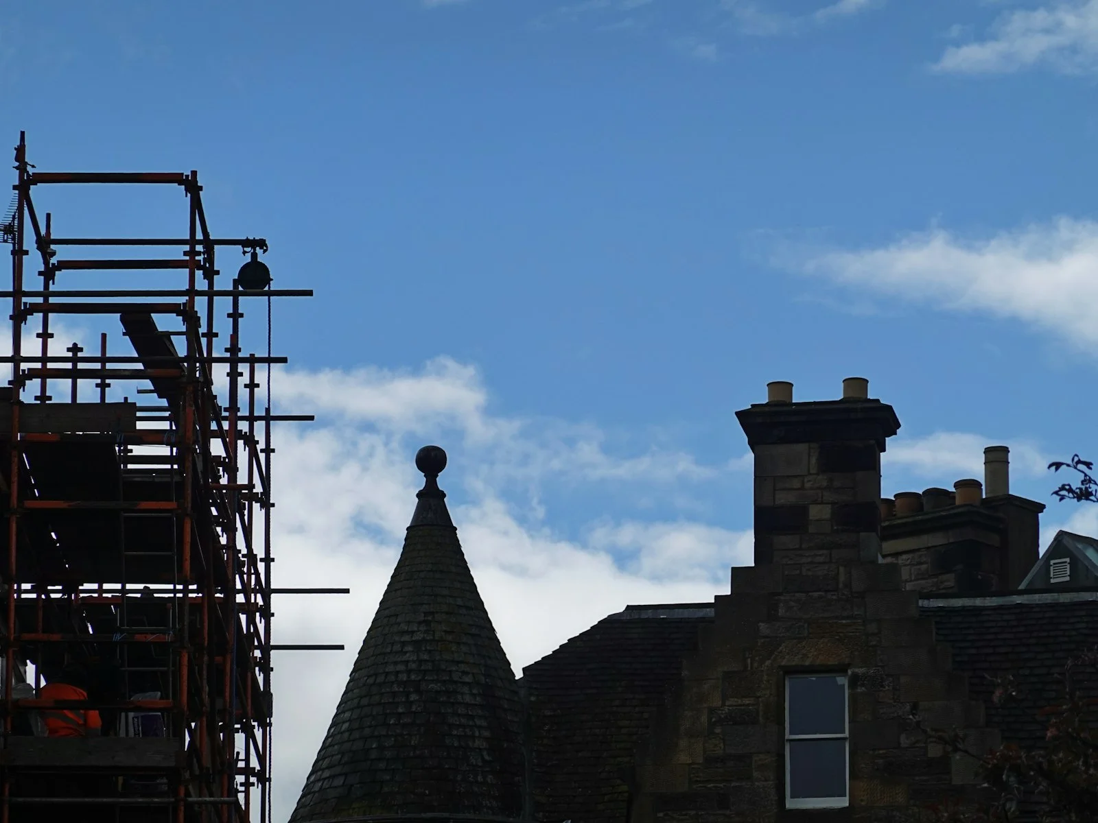 Scaffolding beside a stone building with a conical roof and chimney against blue sky Scaffolding beside a stone building with a conical roof and chimney against blue sky